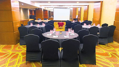 Conference room at Pride Plaza Ahmedabad, featuring a U-shaped arrangement of tables with red tablecloths, chairs, and a projector screen, ideal for business meetings and presentations.